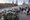 Une énorme pile de fleurs, de photographies et de messages se trouve sur un pont à côté d’une route. Des gens marchent sur le pont. Certaines personnes regardent la pile d’objets-souvenirs. Une femme prend une photographie avec sa tablette. En arrière-plan, on voit un mur de béton rouge (place Rouge à Moscou et une église avec des coupoles courbées (cathédrale Saint-Basile).