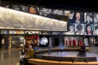 Cinq personnes dans une galerie du Musée. Deux personnes sont assises sur un banc. Trois personnes, dont l'une est en fauteuil roulant, sont dans une zone circulaire où des bulles de lumière colorée sont projetées sur le plancher.