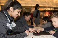 A Museum staff member helping a young child place coloured dots in the shape of braille letters.