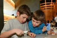 Two young boys holding markers and small cards with string and reading one of the cards.
