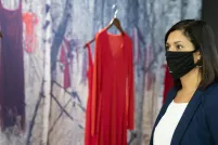 Une femme portant un masque noir se tient devant une exposition du Musée composée de robes rouges suspendues devant un fond de forêt.