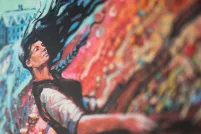 Une femme aux cheveux noirs semble se trouver dans une tempête de vent abstraite et colorée, avec du rouge et du bleu.