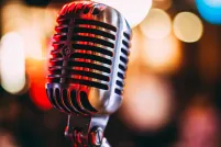 Un microphone au premier plan reflète des lumières rouges et dorées. Des lumières de patio sont floues à l’arrière-plan.