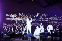 Image fixe d’une animation montrant des silhouettes humaines écrivant « bienvenue » en plusieurs langues en blanc et jaune sur un mur violet.