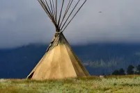 Un grand tipi dans un champ d’herbe. Les perches du tipi s’élèvent dans le ciel brumeux.