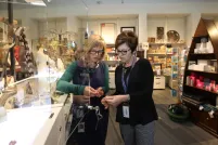 Deux femmes regardent un bijou. Elles sont debout dans un magasin rempli de marchandises colorées.