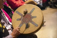 Lors d’un rassemblement culturel, la main d’un aîné tient un tambour à main autochtone peint et son bâton.