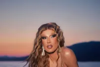 Une personne aux longs cheveux blonds crêpés, assise sur une corniche surplombant une grande étendue d'eau et vêtue d'un bikini doré.