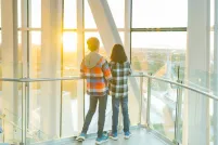 Deux enfants se tiennent dans une tour, dos à la caméra, et regardent vers l’horizon qui surplombe un paysage urbain.