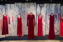 Cinq robes rouges, représentant des femmes et des filles autochtones disparues et assassinées, sont suspendues en rang dans la galerie Les parcours canadiens dans le cadre d’une exposition intitulée « Trouver de la force dans la tristesse ». Derrière les robes, la scène d’une forêt enneigée avec d’autres robes rouges accrochées aux branches des arbres est présentée sur une série de bannières.