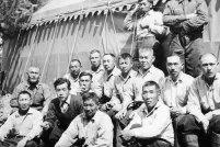 Un groupe d’hommes pose pour une photo avec une grande tente et un arbre en arrière-plan.