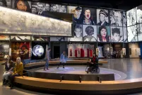 Deux personnes sont assises sur un banc. Trois personnes, dont l'une est en fauteuil roulant, sont dans une zone circulaire où des bulles de lumière colorée sont projetées sur le plancher.