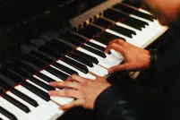 Deux mains jouent sur les touches d’un piano Yamaha d’un noir étincelant. La personne au piano, que l’on voit à peine, porte un haut noir à manches longues.