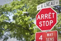 Un panneau d’arrêt et un panneau de signalisation de rue, en français et en anglais, se trouvent devant des arbres.