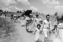 Des femmes et des enfants transportant des fardeaux sur leur tête marchent le long d’un chemin de terre.