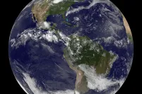 Une vue panoramique de la Terre depuis l’espace, centrée sur l’Amérique du Nord et l’Amérique du Sud, avec des nuages blancs tourbillonnant au-dessus d’océans bleus et de masses continentales vertes et brunes.
