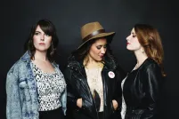 Trois femmes posent devant un mur noir.