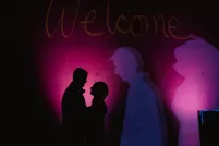 Les silhouettes d’un homme et d’une femme qui se font face et se tiennent devant un mur sombre éclairé de taches de lumière violette.