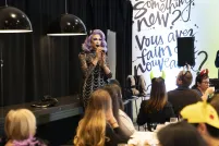 Une artiste de drag aux cheveux violets et à la robe argentée et noire s'exprime devant un groupe qui brunch.