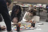Deux jeunes enfants sont assis côte à côte à une table ronde, occupés à une activité artistique avec des marqueurs et des crayons de couleur.