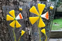 Deux décorations en verre fusionné représentant des fleurs jaunes sont placées dans un pot à fleurs à l’extérieur.