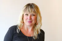 Un homme souriant aux yeux verts porte un chapeau haut de forme en feutre rouge et une chemise à col ivoire avec des boutons-pression noirs.