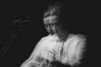 Photo en noir et blanc de Sarah Harmer jouant de la guitare. Deux images floues semblent juxtaposées l’une sur l’autre.