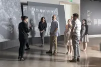 Un petit groupe de gens debout devant de grands écrans sur lesquels on voit des photographies. Ils regardent une femme qui leur parle.