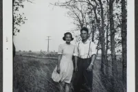 Un jeune couple canadien d’origine japonaise pose dans un champ avec des arbres en arrière-plan.