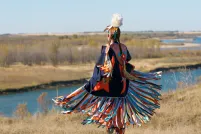 Une danseuse autochtone vêtue d’un châle d’apparat aux couleurs vives, près d’une rivière.