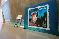 Un grand affichage d'un timbre représentant le sergent Tommy Prince est visible sur le côté droit de l'image. Une passerelle située devant le panneau d'affichage mène à gauche de l'image, dans la galerie Perspectives indigènes.