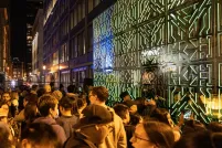 Beaucoup de gens se tiennent entre deux miroirs joints aux motifs complexes qui reflètent les lumières vertes et une foule de spectateurs.