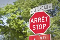 Un panneau d’arrêt et un panneau de signalisation de rue, en français et en anglais, se trouvent devant des arbres.
