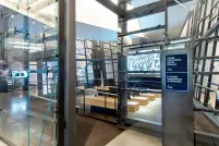 Des parois de verre inégales entourent une salle de projection avec un écran et 4 bancs en face. À l’extérieur de l’entrée de la salle, un panneau indique le film sélectionné.