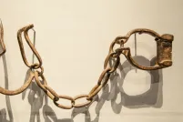 Des menottes rouillées sont suspendues sur un mur blanc.