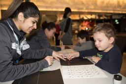 A Museum staff member helping a young child place coloured dots in the shape of braille letters.