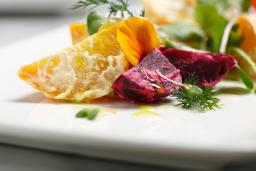 Des quartiers de pommes de terre dorés sont disposés artistiquement sur une assiette blanche carrée, avec des feuilles vertes, des quartiers de betteraves rouges et des garnitures.