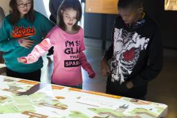 Un groupe de trois enfants se tient devant une table interactive.