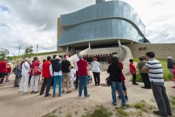 Un groupe de personnes regardant une chorale qui chante sur les marches de l’amphithéâtre extérieur du Musée.