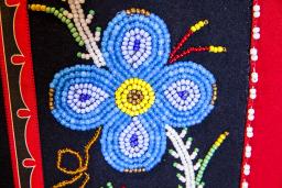 A blue beaded flower on a black and red background. 