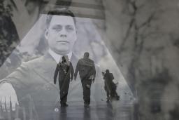 Une image historique translucide d’un homme en complet superposé à une photo contemporaine de deux hommes en silhouette marchant dans un corridor triangulaire.