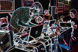 Quatre personnes autour d’une table recouverte d’ordinateurs et d’équipement de musique électronique. La photo a été modifiée de façon à ce que l’arrière-plan soit noir et les éléments de la photo, surlignés en néon multicolore.