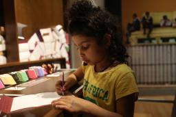 Une fille écrivant sur une feuille de papier avec un crayon.