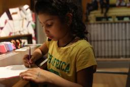 Une fille écrivant sur une feuille de papier avec un crayon.