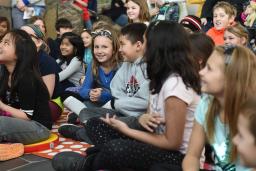 Smiling children sitting cross-legged on the floor. One girl in the centre is looking into the camera.