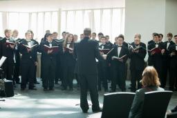 Une chorale d’hommes habillés de noir, tenant des livres et chantant devant un chef de chœur.