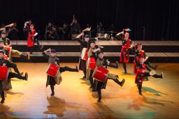 Une troupe de percussionnistes qui danse sur une scène. Les tambours et certains éléments des costumes sont rouge vif.