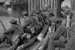 Un groupe de soldats armés regarde passer un char d’assaut.