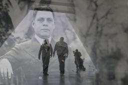Une image historique translucide d’un homme en complet superposé à une photo contemporaine de deux hommes en silhouette marchant dans un corridor.