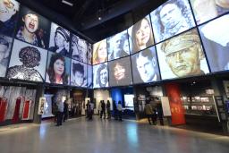 The museum's Canadian Journeys gallery, seen from the perspective of a visitor standing in the middle of it, surrounded by niches that share stories of Canadian experiences of human rights. On the walls above the niches, large images of faces of Canadian human rights defenders are seen arranged in a grid pattern.